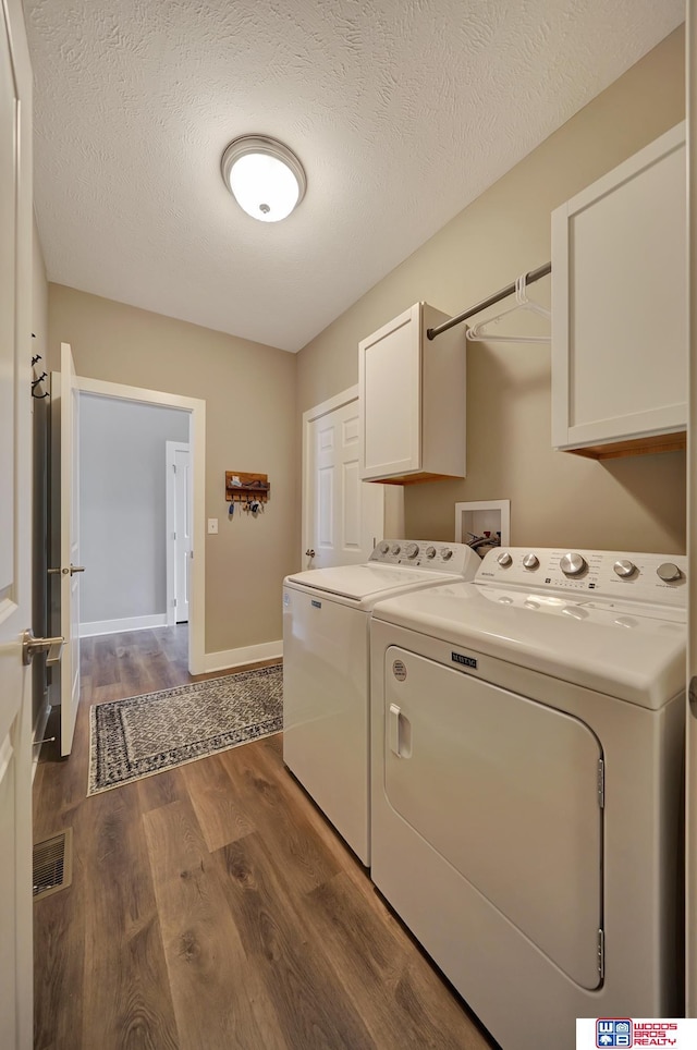 laundry room featuring washing machine and dryer, dark hardwood / wood-style flooring, cabinets, and a textured ceiling