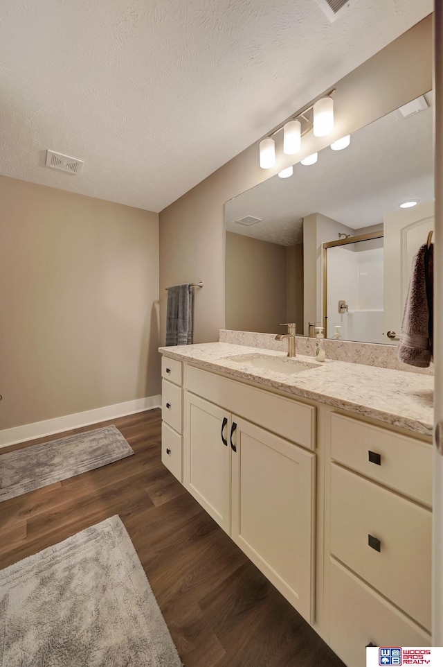 bathroom featuring hardwood / wood-style floors, vanity, a shower with shower door, and a textured ceiling