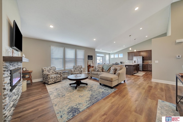 living room featuring a stone fireplace, lofted ceiling, and hardwood / wood-style flooring