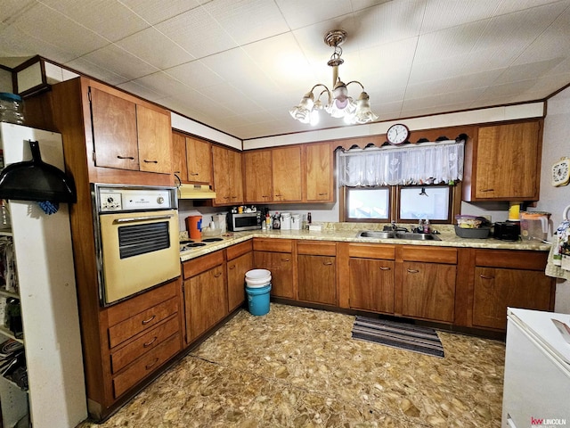 kitchen with a chandelier, pendant lighting, white appliances, and sink