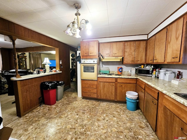 kitchen with hanging light fixtures, an inviting chandelier, white oven, kitchen peninsula, and wooden walls