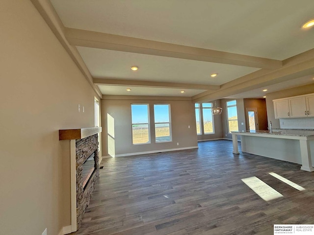 unfurnished living room featuring dark hardwood / wood-style flooring, beam ceiling, a stone fireplace, and sink