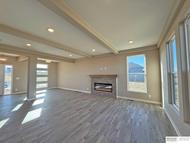 unfurnished living room featuring hardwood / wood-style flooring, a stone fireplace, beamed ceiling, and an inviting chandelier