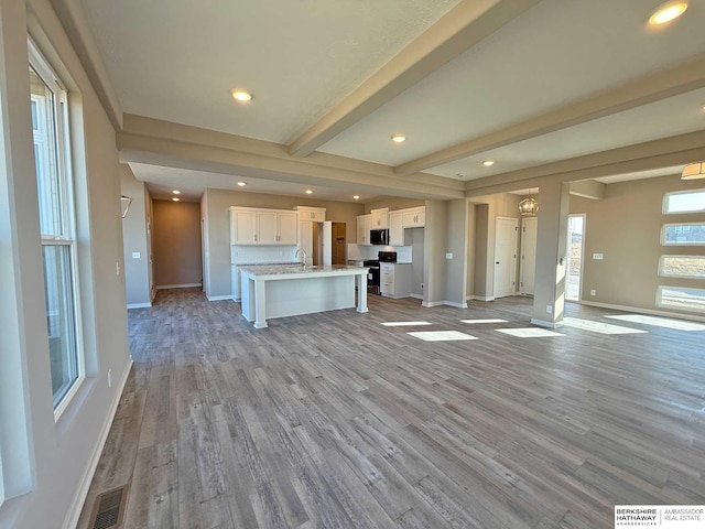 unfurnished living room featuring sink, beamed ceiling, and light hardwood / wood-style floors