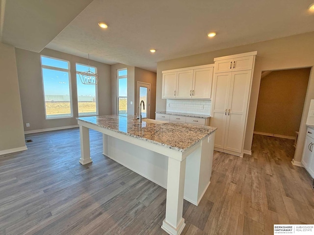 kitchen with a center island with sink, white cabinets, hardwood / wood-style flooring, decorative backsplash, and light stone counters