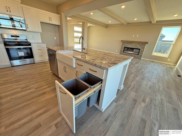 kitchen with beamed ceiling, stainless steel appliances, white cabinets, and a kitchen island with sink