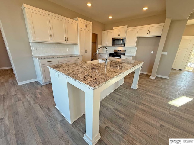 kitchen with a kitchen island with sink, sink, light stone counters, white cabinetry, and stainless steel appliances