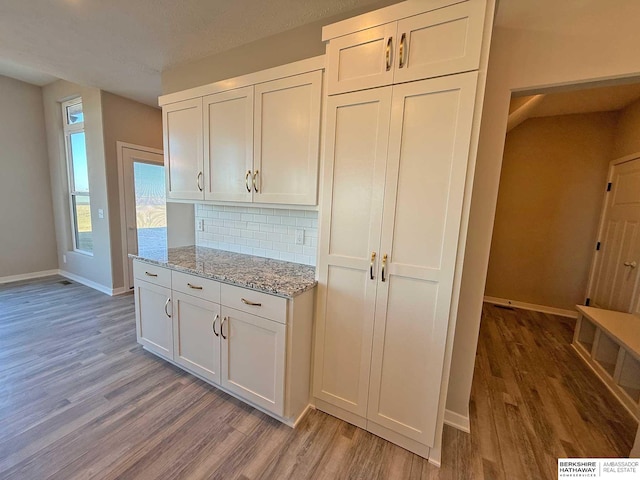 kitchen featuring decorative backsplash, white cabinets, light stone counters, and light wood-type flooring