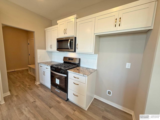 kitchen featuring light wood-type flooring, tasteful backsplash, light stone counters, stainless steel appliances, and white cabinets