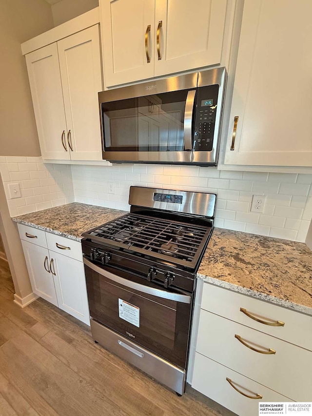 kitchen featuring light hardwood / wood-style flooring, appliances with stainless steel finishes, tasteful backsplash, light stone counters, and white cabinetry