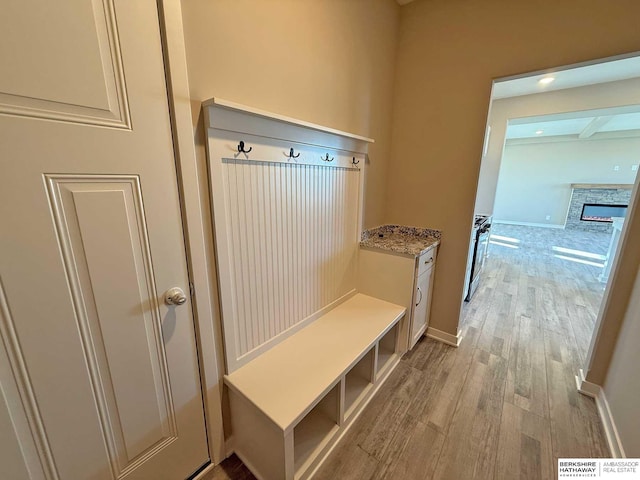 mudroom featuring beamed ceiling, light hardwood / wood-style floors, and a stone fireplace