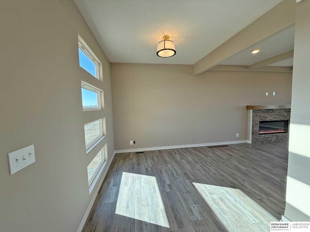 interior space with beamed ceiling, hardwood / wood-style flooring, a stone fireplace, and plenty of natural light