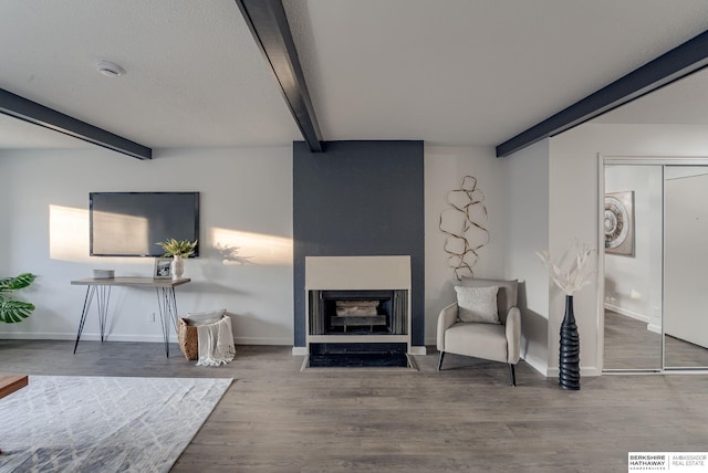 living area with beamed ceiling, a fireplace, and hardwood / wood-style flooring