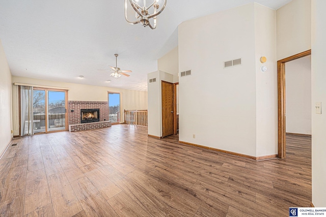 unfurnished living room featuring ceiling fan with notable chandelier, hardwood / wood-style flooring, a brick fireplace, and high vaulted ceiling