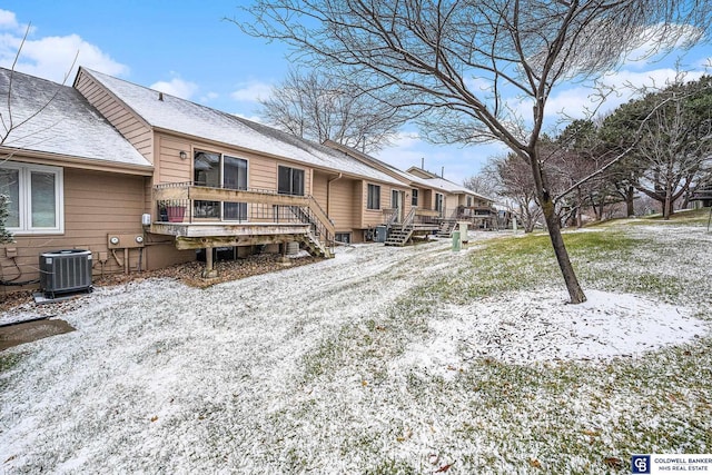 snow covered house featuring cooling unit and a wooden deck