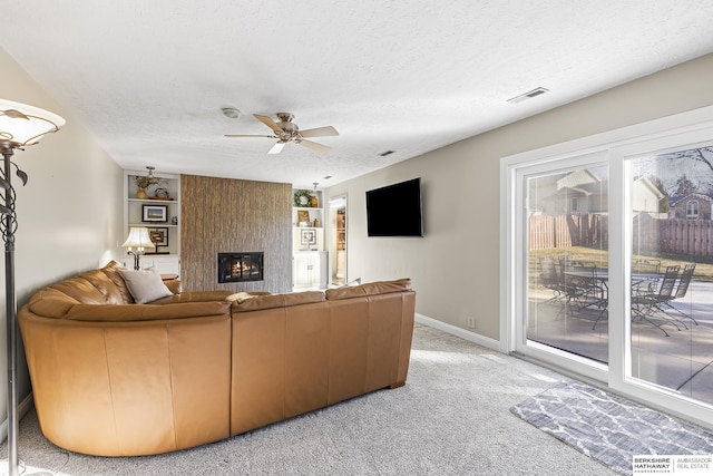 carpeted living room featuring a textured ceiling, ceiling fan, a fireplace, and built in features