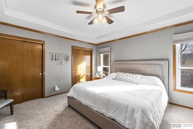 carpeted bedroom featuring a textured ceiling, two closets, ceiling fan, and a tray ceiling