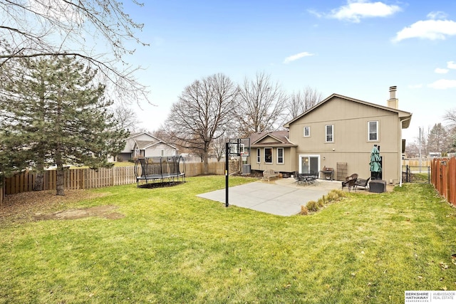 rear view of property featuring a lawn, a patio area, and a trampoline