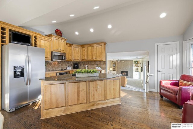 kitchen featuring appliances with stainless steel finishes, vaulted ceiling, dark stone countertops, backsplash, and dark wood-type flooring