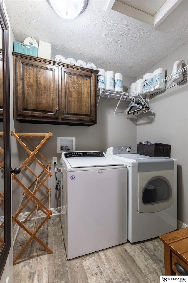 laundry area with washer and dryer, cabinets, a textured ceiling, and light hardwood / wood-style flooring