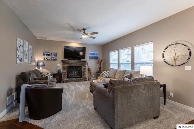 living room featuring a stone fireplace, ceiling fan, and carpet floors