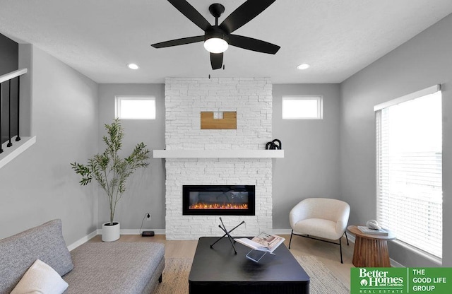 living room featuring a wealth of natural light, a fireplace, ceiling fan, and light hardwood / wood-style floors