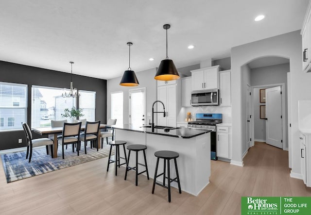 kitchen with appliances with stainless steel finishes, sink, a center island with sink, an inviting chandelier, and white cabinets