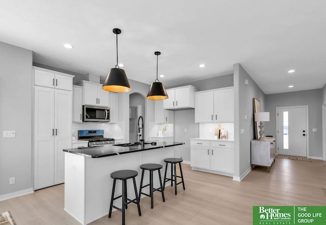 kitchen with appliances with stainless steel finishes, pendant lighting, a center island with sink, light hardwood / wood-style flooring, and white cabinetry