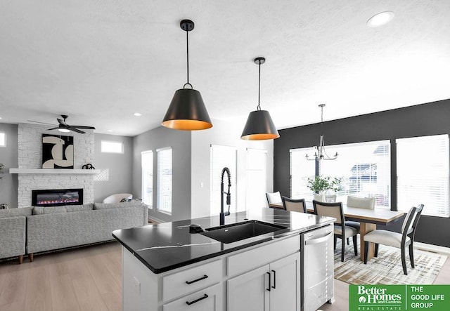 kitchen with white cabinets, sink, stainless steel dishwasher, a fireplace, and decorative light fixtures