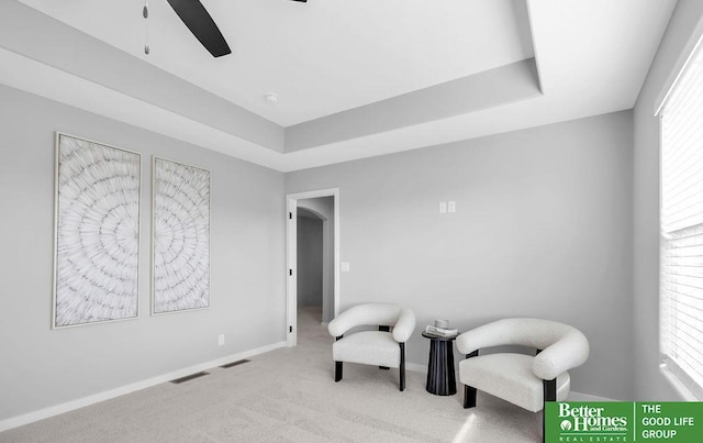 living area featuring a raised ceiling, ceiling fan, and light colored carpet