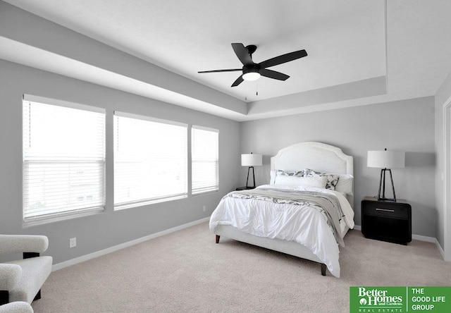 bedroom with light carpet, multiple windows, a tray ceiling, and ceiling fan