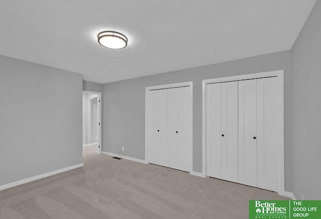 unfurnished bedroom with multiple closets and light carpet