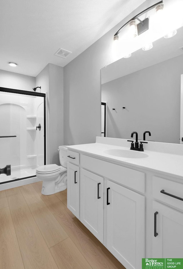 bathroom featuring wood-type flooring, vanity, toilet, and a shower with shower door