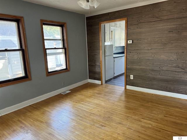 unfurnished room with wood walls, light hardwood / wood-style flooring, and ceiling fan