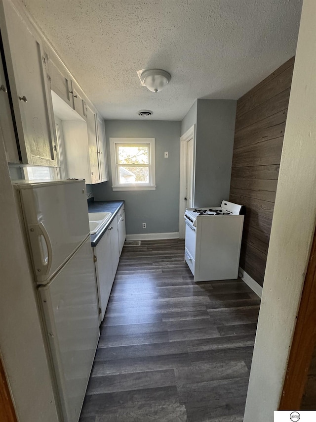 kitchen with white cabinetry, dark hardwood / wood-style flooring, white appliances, and wooden walls