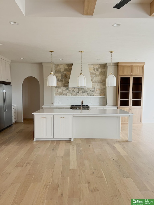 kitchen featuring high end refrigerator, a center island with sink, white cabinets, and decorative light fixtures