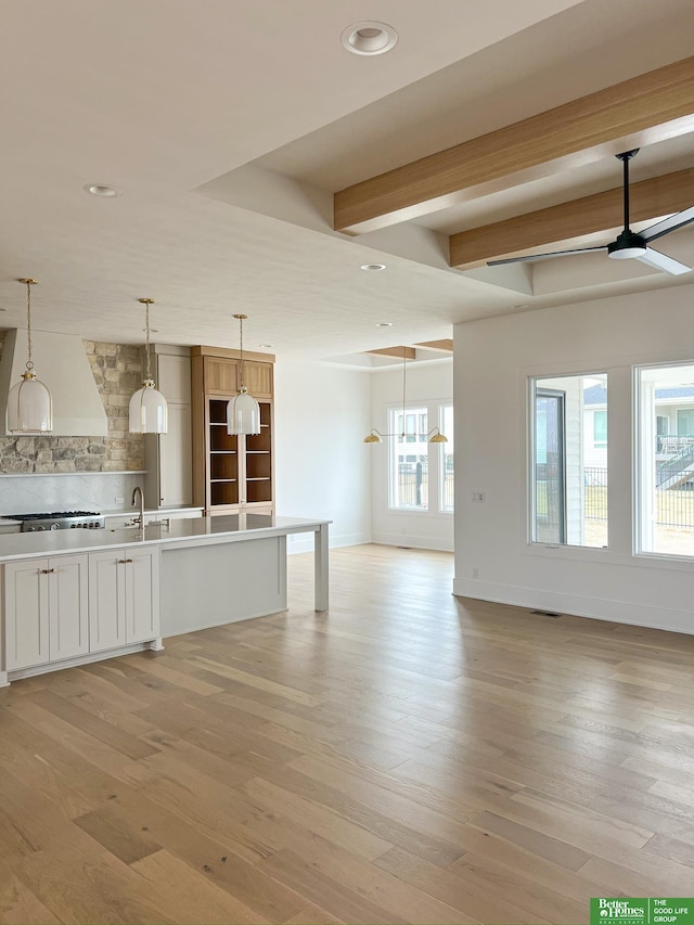 unfurnished living room with beam ceiling, ceiling fan, light hardwood / wood-style flooring, and sink