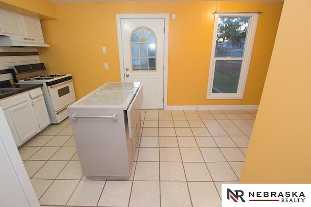 kitchen featuring white gas stove, tasteful backsplash, white cabinets, light tile patterned flooring, and exhaust hood