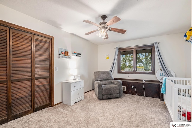 bedroom with ceiling fan, a textured ceiling, light colored carpet, a crib, and a closet