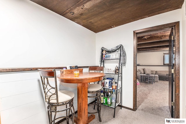 dining area featuring light colored carpet, wooden ceiling, and bar area