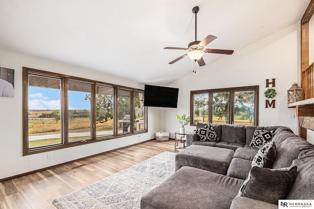 living room with ceiling fan, a stone fireplace, lofted ceiling, and light hardwood / wood-style flooring