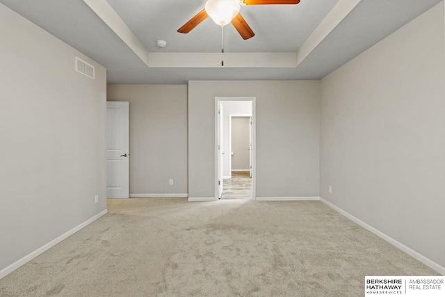 unfurnished bedroom with ceiling fan, a raised ceiling, and light carpet