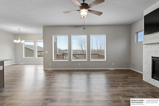 unfurnished living room featuring ceiling fan with notable chandelier, dark hardwood / wood-style floors, and a stone fireplace