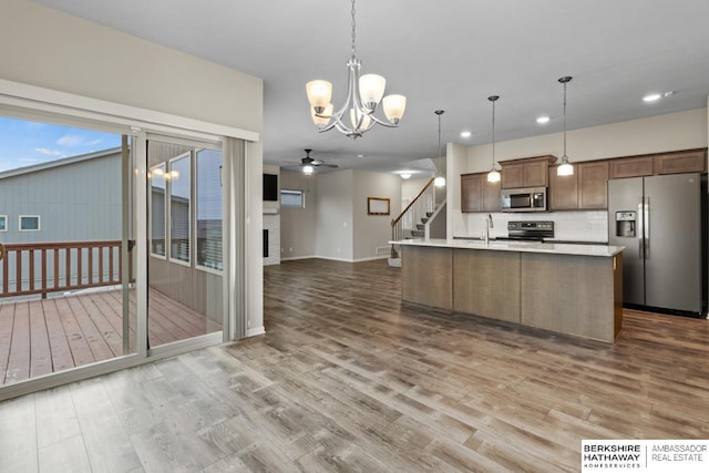 kitchen featuring ceiling fan with notable chandelier, hardwood / wood-style flooring, an island with sink, decorative light fixtures, and stainless steel appliances