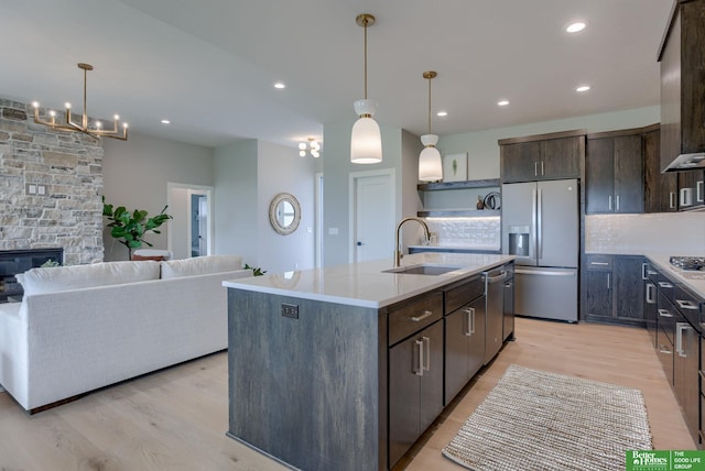 kitchen with dark brown cabinetry, sink, stainless steel appliances, decorative backsplash, and a center island with sink