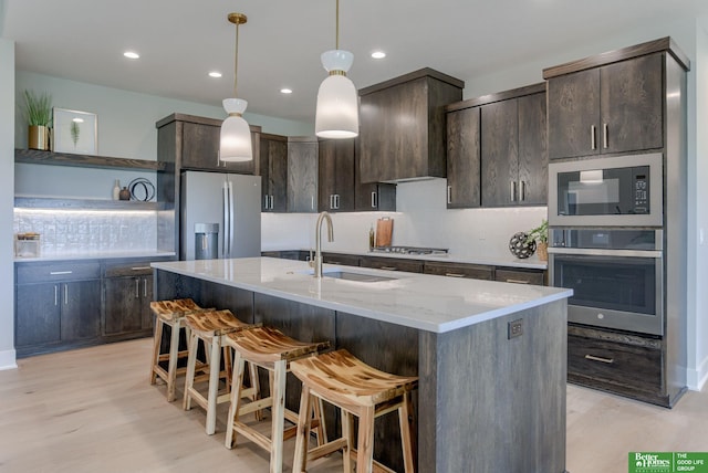 kitchen featuring light stone counters, dark brown cabinetry, ventilation hood, stainless steel appliances, and a center island with sink