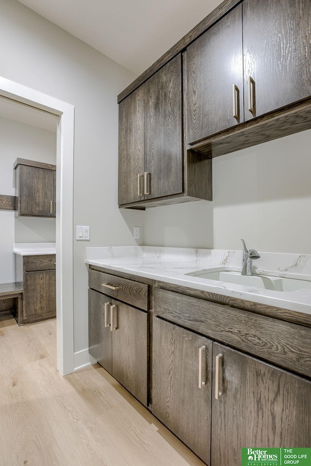 kitchen with sink, light hardwood / wood-style flooring, dark brown cabinetry, and light stone counters