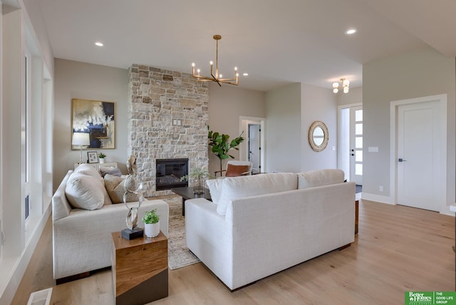 living room featuring a fireplace, light wood-type flooring, and an inviting chandelier