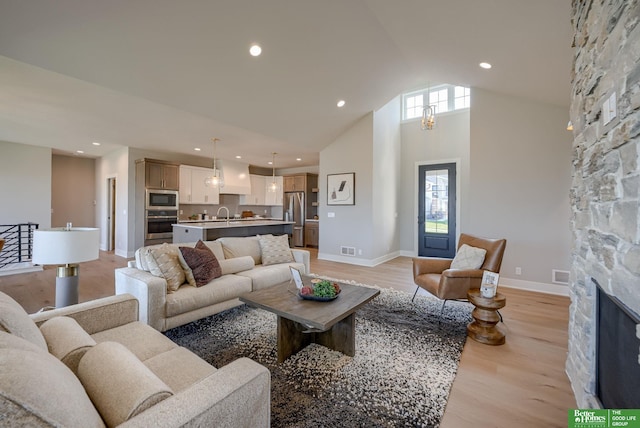 living room featuring light hardwood / wood-style floors, a stone fireplace, sink, and a high ceiling