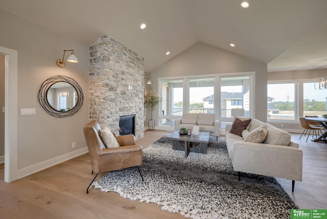 living room featuring light wood-type flooring, a stone fireplace, plenty of natural light, and vaulted ceiling